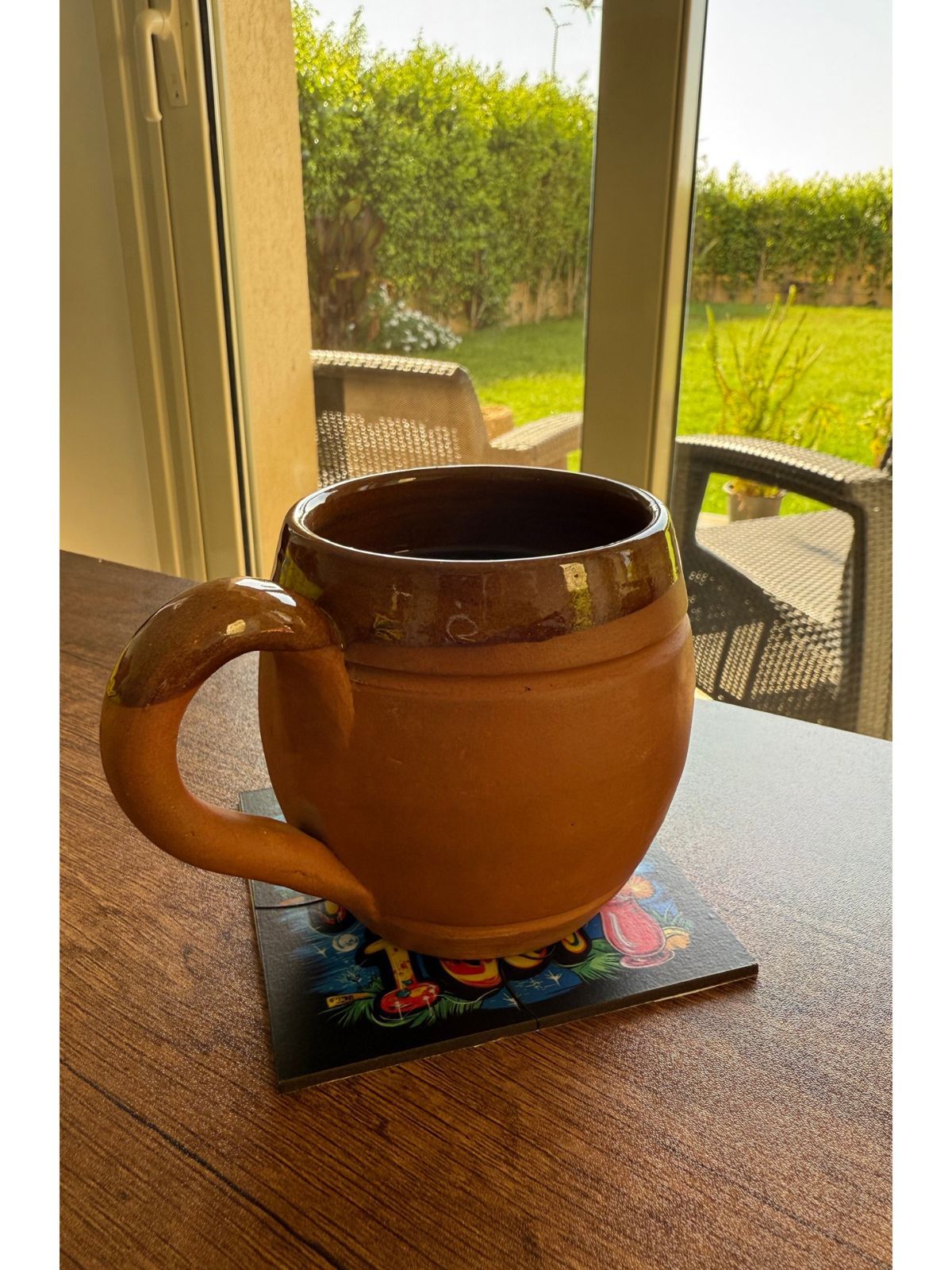 Terracotta mug on a coaster with a garden view outside a window