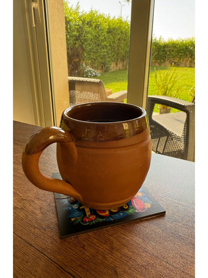Terracotta mug on a coaster with a garden view outside a window