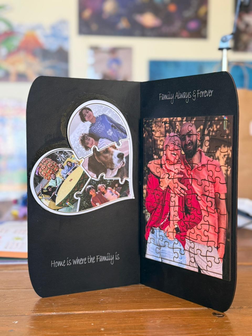 A black personalized photo collage keepsake box standing open on a wooden table, showing printed photos, puzzle pieces, and handwritten text on the inside cover.